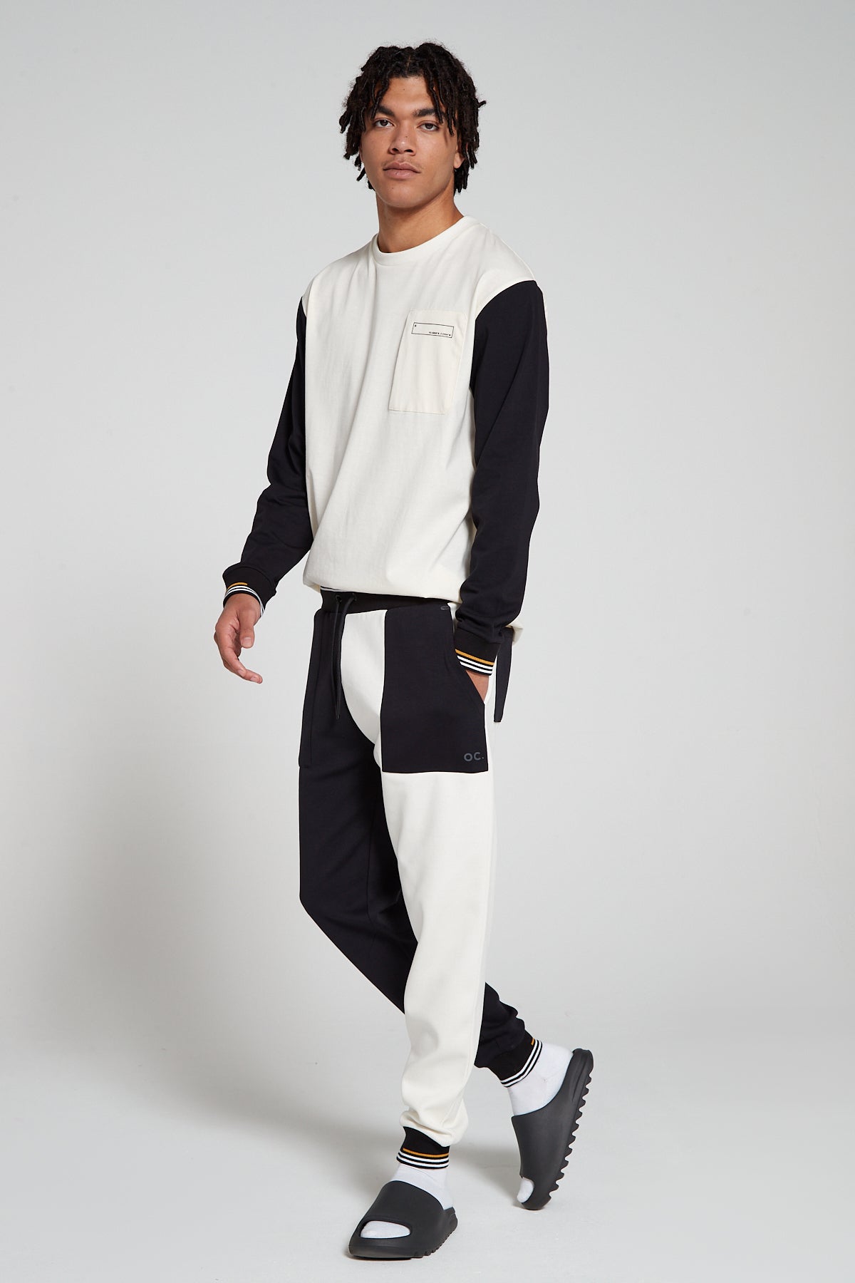 Full look of a model wearing Original Creator Classic Jet black Color with one leg in jet black and the other leg in off white white color. Model is highlighting the combination with long sleeve off white T shirt with black sleeves to match with white and black joggers style.
