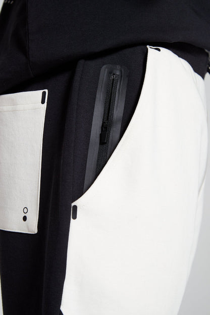 A side angle and close up view of Original Creator Jet Black zip pocket shorts with four side pockets. The shorts feature a color combination of off white and Black and zip pockets