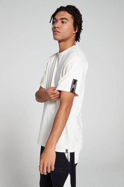 Model looking away showing side view wearing Original Creator Reflection T-Shirt in Off White color with reflection written near the round neck and highlighting brand taping on the left sleeve