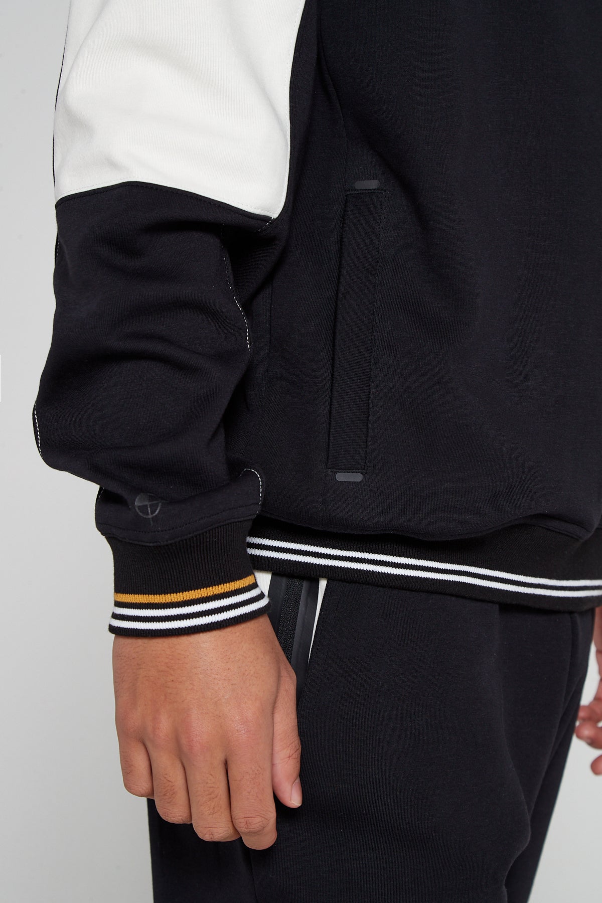 Close up bottom right view of oversized Original Creator Retro Zip pocket Sweatshirt in Jet Black color with black zip pocket on the side. Model is showing off the unique yellow and white on wrists of sweatshirt