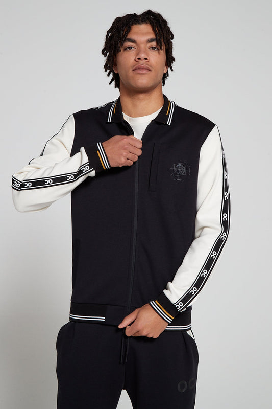 Front view of a model wearing an Original Creator Zip Jacket in black and white color. Model is closing the zipper Showing off the OC signature taping on the sleeves. 