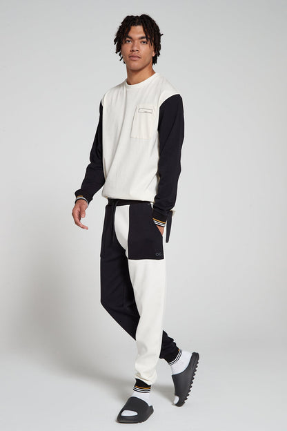 Full look of a model wearing Original Creator Classic Jet black Color with one leg in jet black and the other leg in off white white color. Model is highlighting the combination with long sleeve off white T shirt with black sleeves to match with white and black joggers style.  