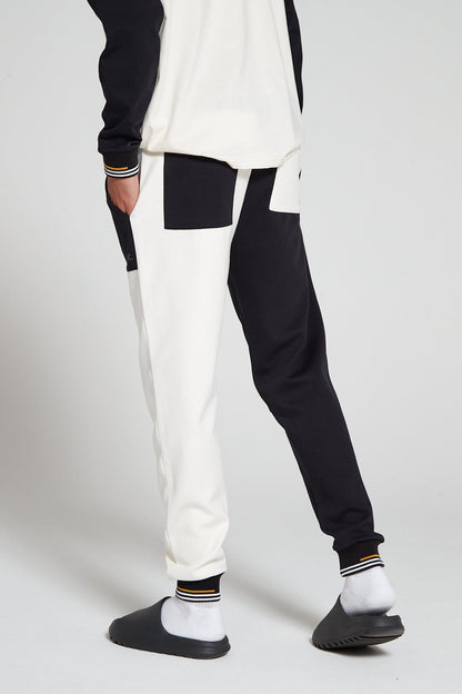 Model showing a behind view wearing Original Creator Track 2.0 Classic Joggers in Jet black Color with one leg in jet black and the other leg in off white color. Two pockets at the back featuring one black pocket on white leg and one white pocket on black leg.
