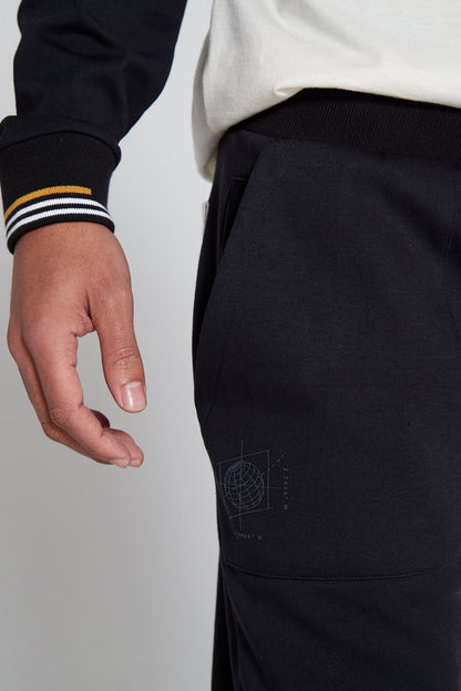 A close up angle of black colored right leg of Original Creator Jet black Classic Joggers includes a zip pocket and regular pocket. Close up shot also highlights globe branding under the pocket on right side.