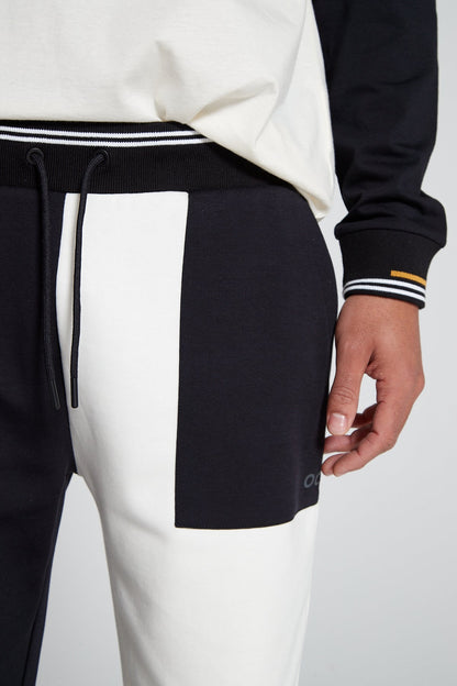 A close up angle of white colored left leg of Original Creator Jet black Classic Joggers includes a zip pocket and regular pocket. Close up shot also highlights OC branding under the pocket on left side.