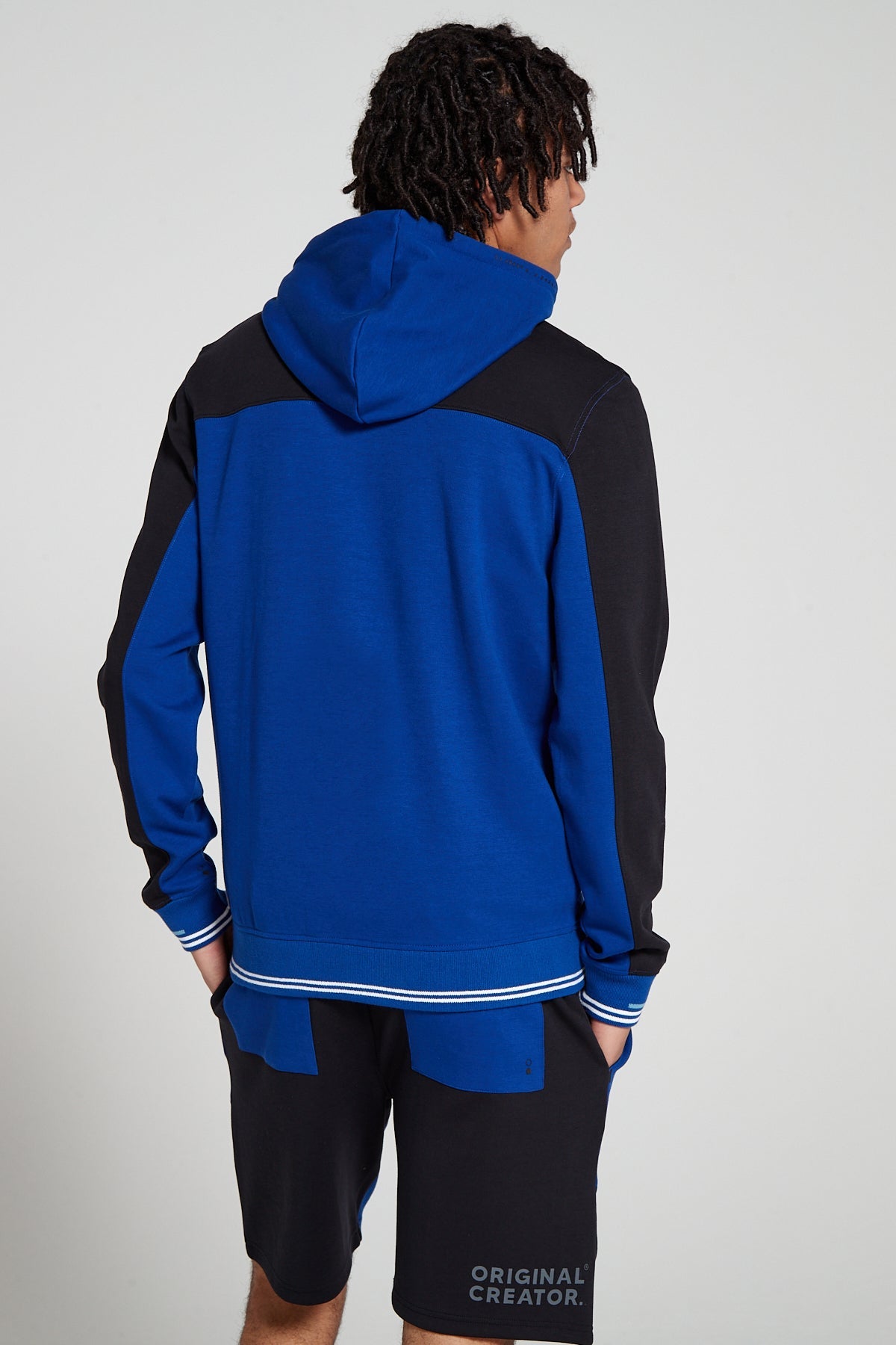 Model showing behind view wearing Original Creator Retro Zip Hoodie in Olympic Blue color with no branding at the back and featuring water repellent technology and classic line pattern on the wrists and color combination of Olympic blue and black