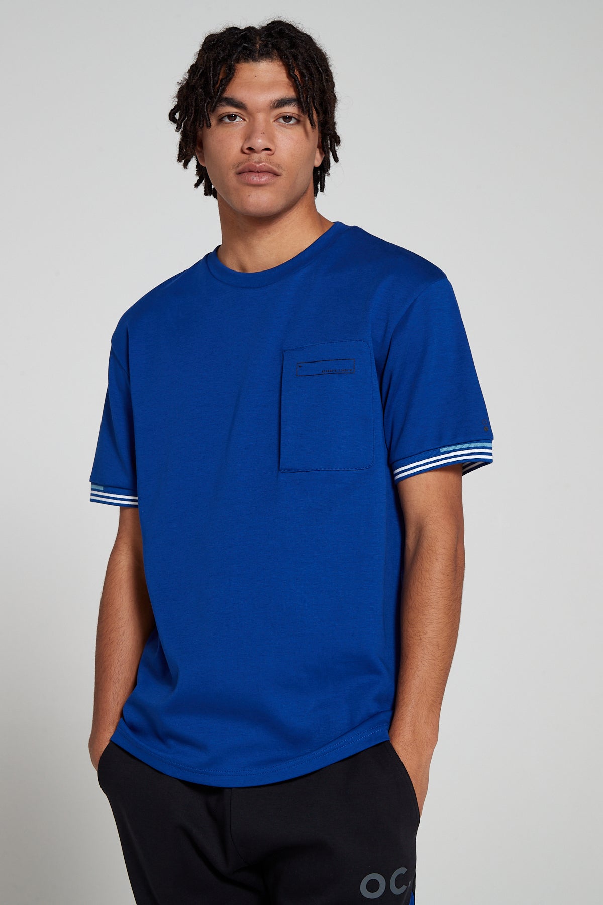 Model looking Straight wearing Original Creator oversized Olympic Blue T shirt with very low branding and features water repellent technology zip pocket 