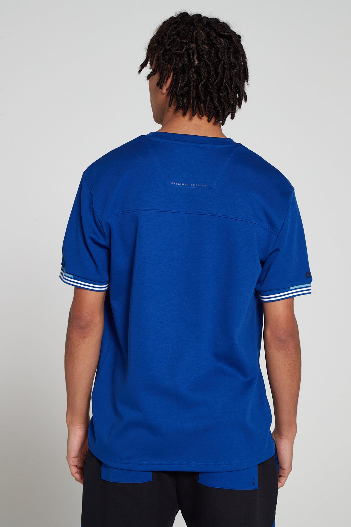 Model showing behind view wearing Original Creator oversized Olympic Blue T shirt with very low branding at the back and features water repellent technology