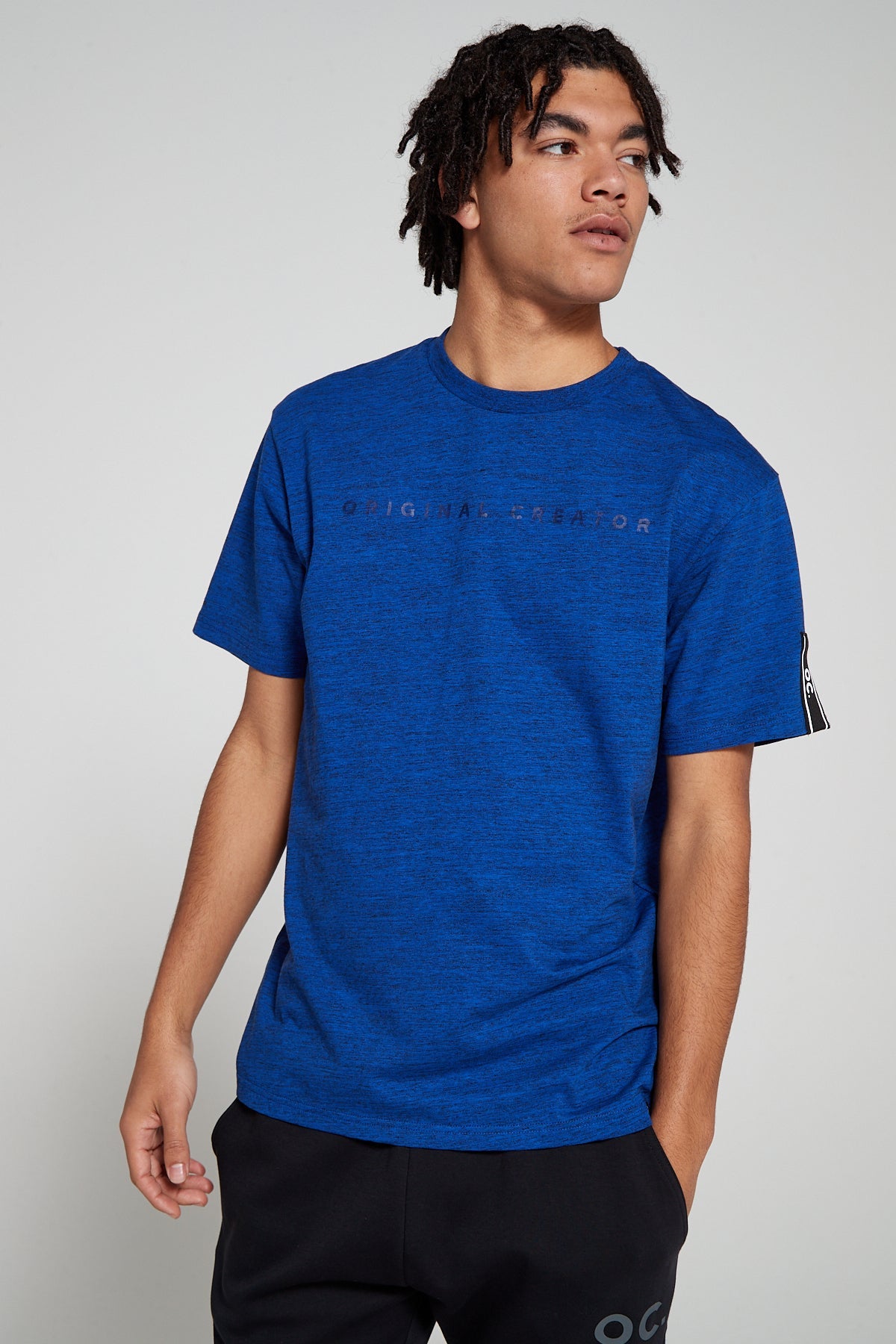 Model looking away wearing Original Creator oversized Blue T shirt with branding on the front. This T shirt features water repellent technology with brand tapping on one sleeve