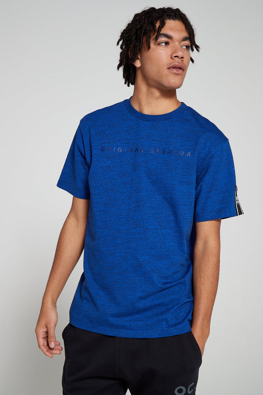 Model looking away wearing Original Creator oversized Blue T shirt with branding on the front. This T shirt features water repellent technology with brand tapping on one sleeve