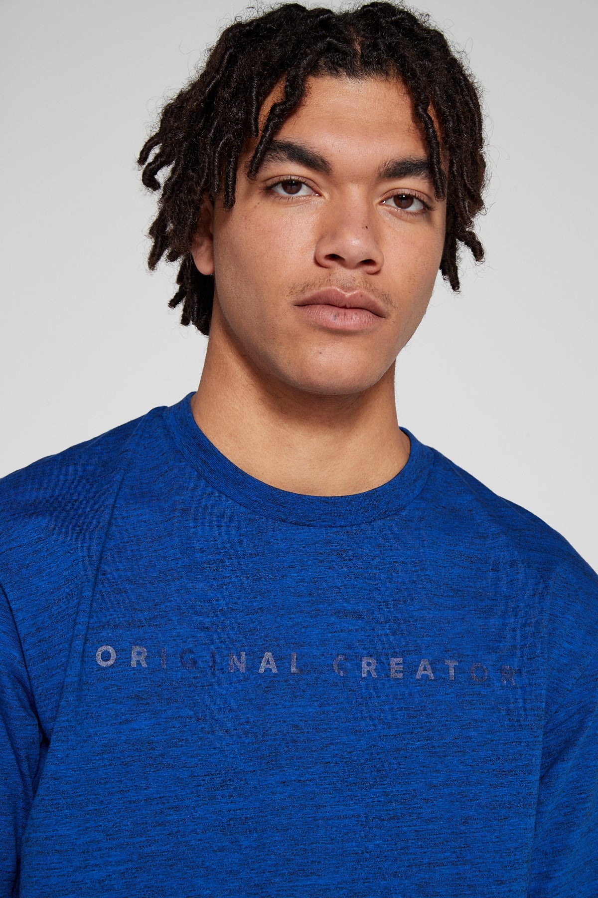 Model looking straight showing close up view wearing Original Creator oversized Olympic Blue T shirt with some branding on the front side and features water repellent technology