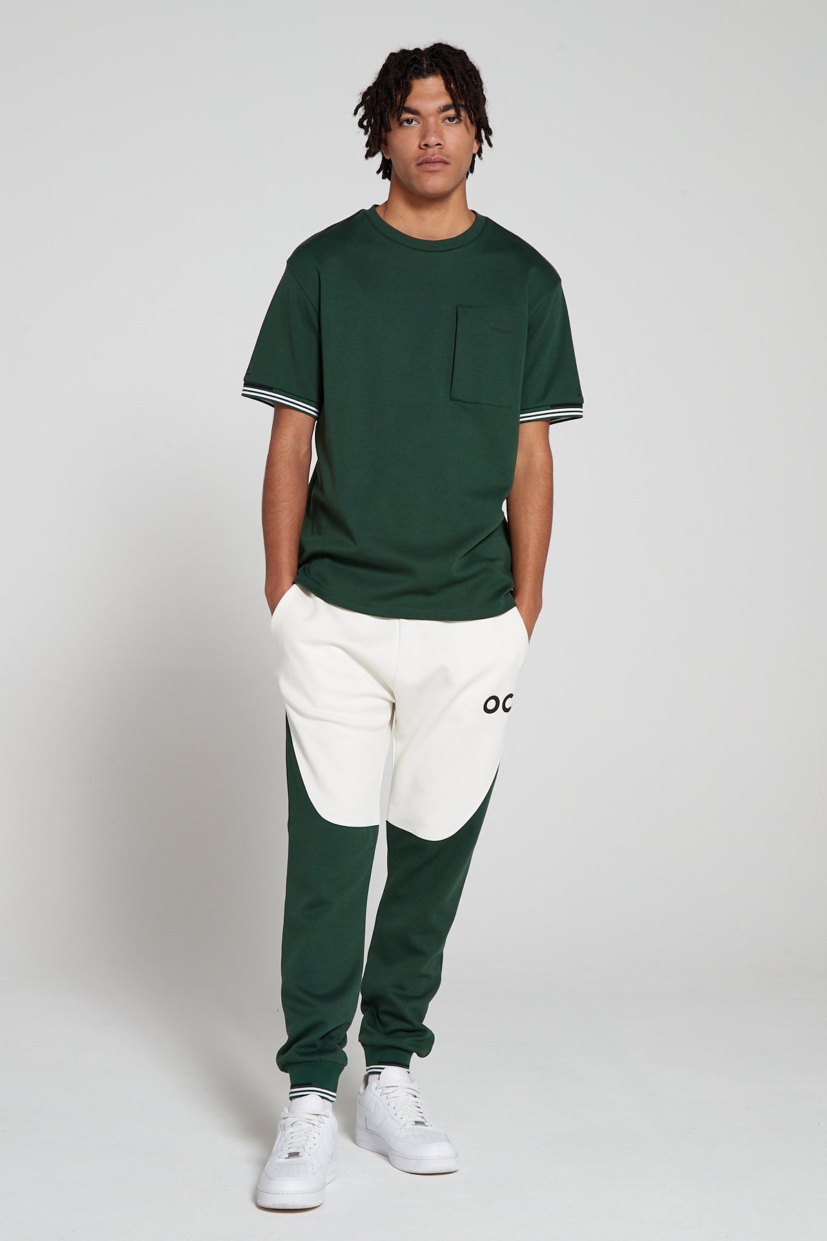 Full look of a model wearing Original Creator oversized green T shirt with very low branding and features water repellent technology zip pocket and wearing Original creator retro joggers