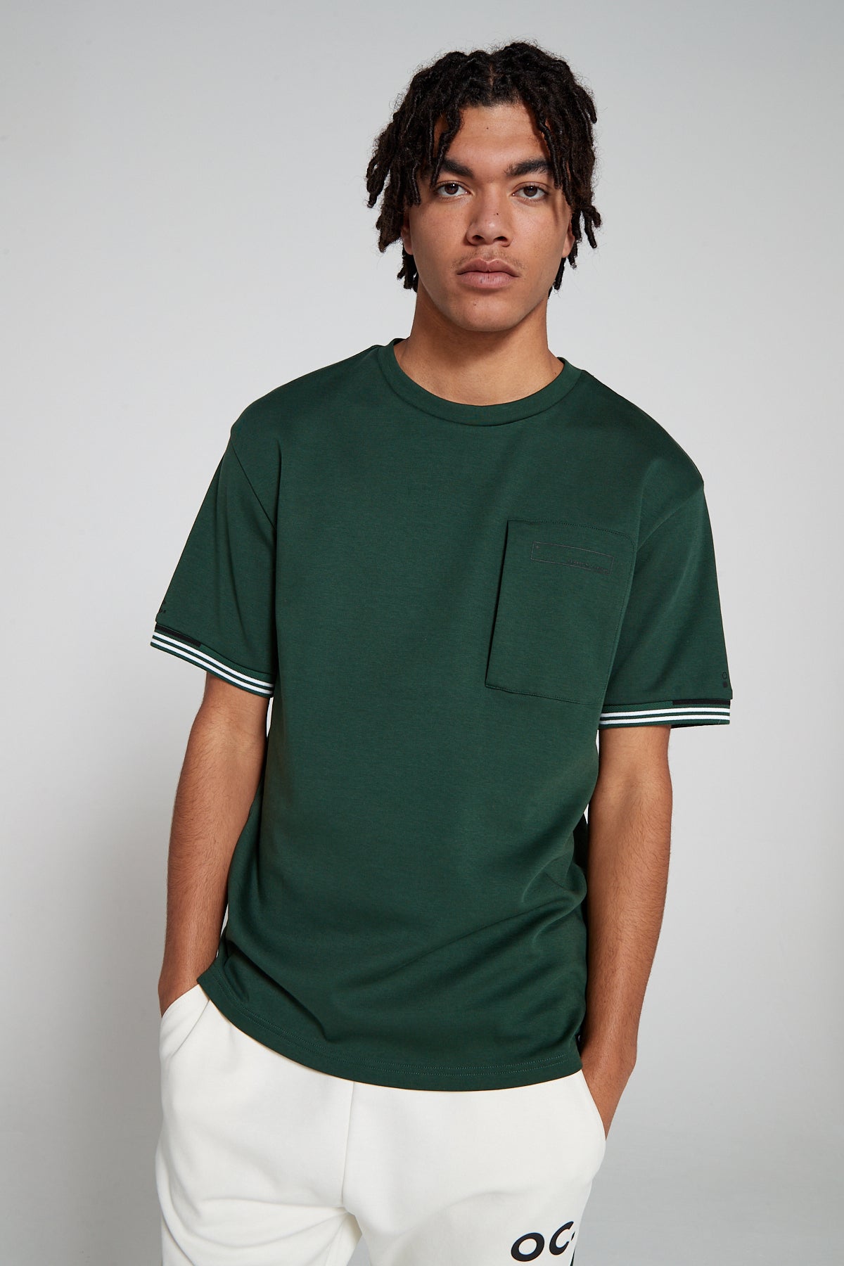 Model looking Straight wearing Original Creator oversized green T shirt with very low branding and features water repellent technology zip pocket and round neck