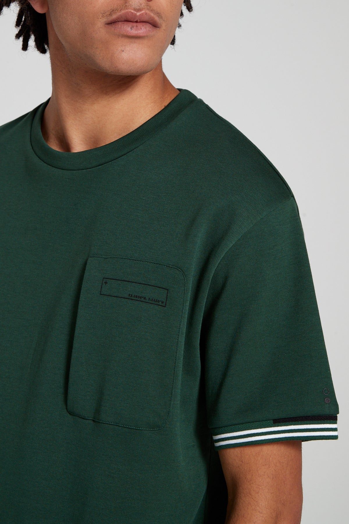 Model looking away showing close up view wearing Original Creator oversized green T shirt with very no branding and features water repellent technology zip pocket and round neck