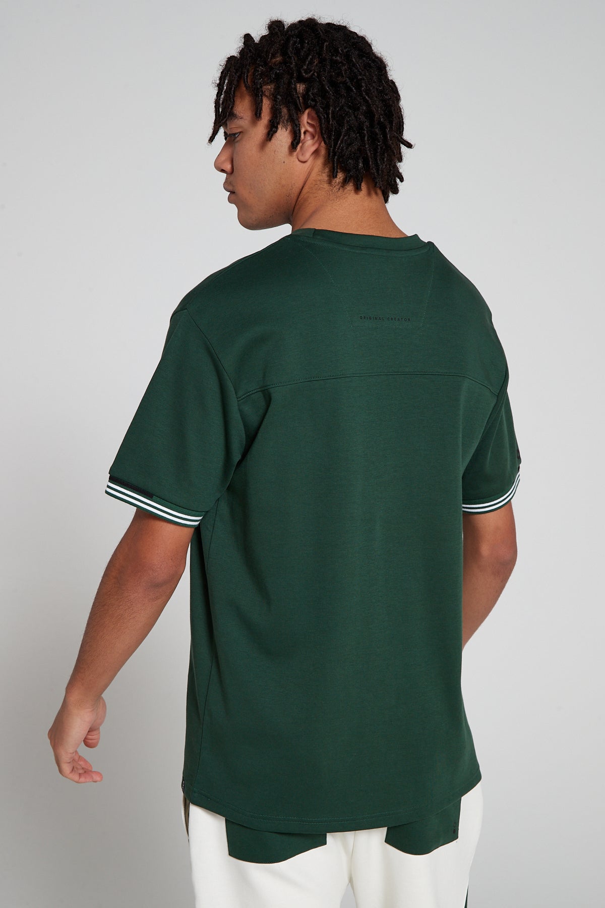 Model showing behind view wearing Original Creator oversized green T shirt with very low branding at the back and features water repellent technology 