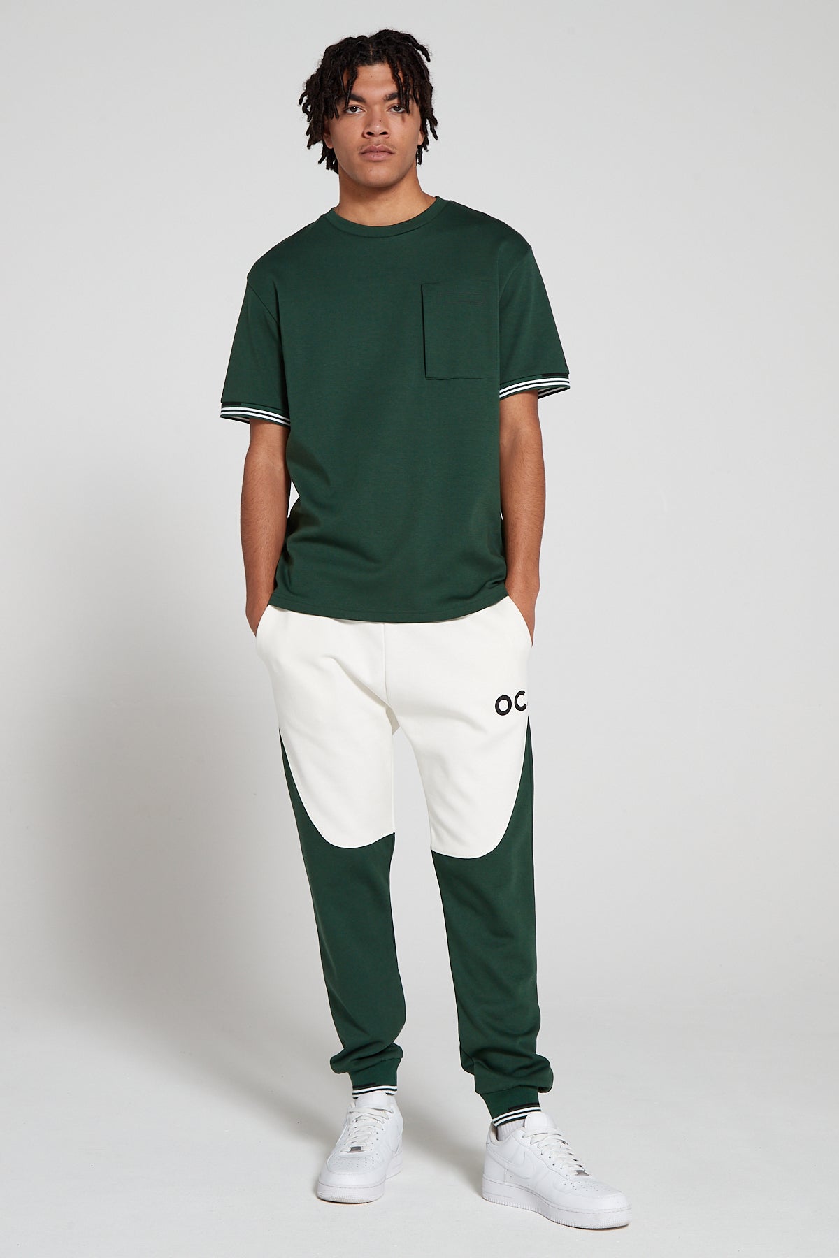 Full look of a model wearing Original Creator Retro Joggers in Varsity Green color featuring a zip pocket green T shirt and putting hands in the Jogger pockets. The joggers are in green and white color.