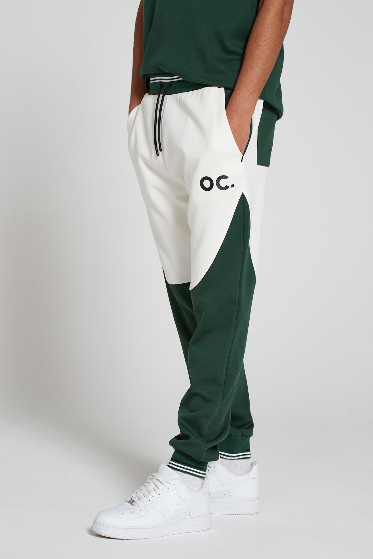 Model has their hands in pockets in a side angle shot of Original Creator Retro Joggers in Varsity green color. Picture also highlights one back pocket one side pocket and one zipper pocket.