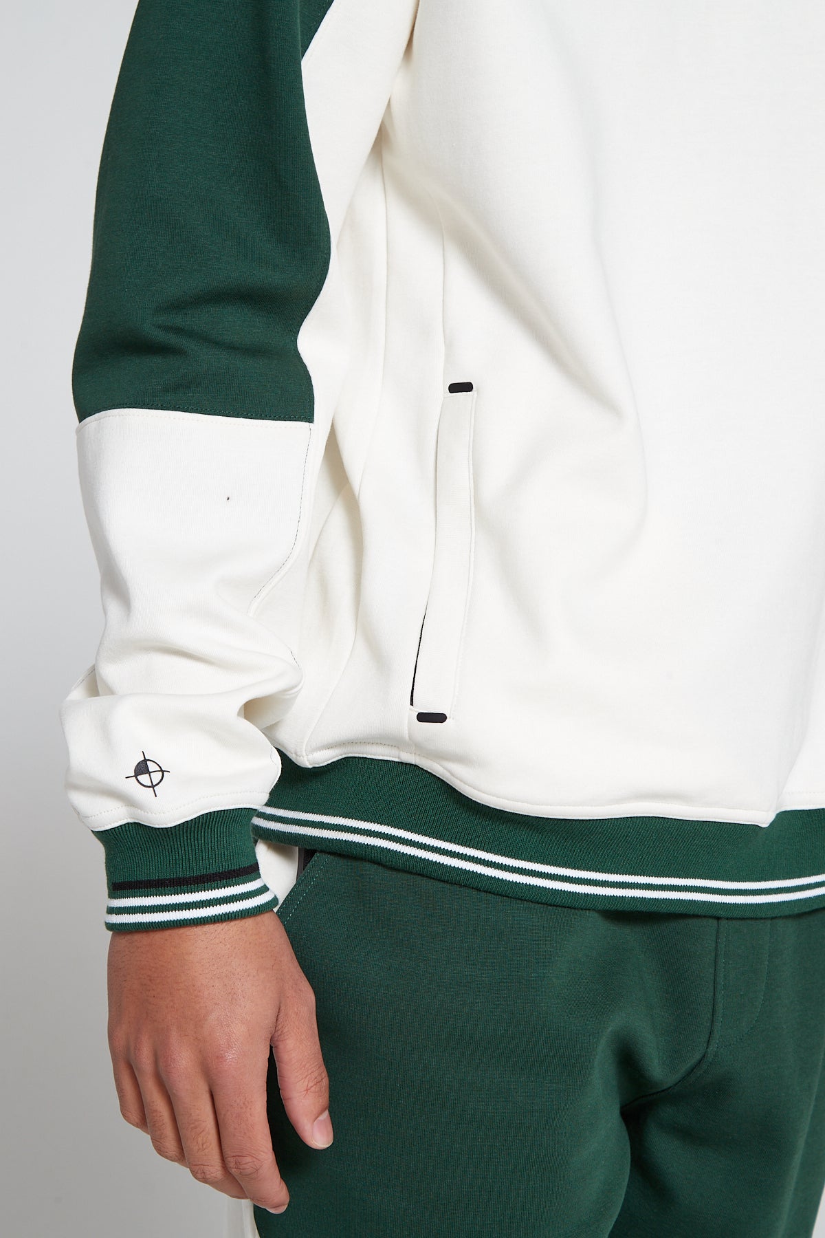 Close up bottom right view of oversized Original Creator Retro Zip pocket Sweatshirt in Varsity Green color with white zip pocket on the side. Model is showing off the unique black and white lining on wrists of sweatshirt