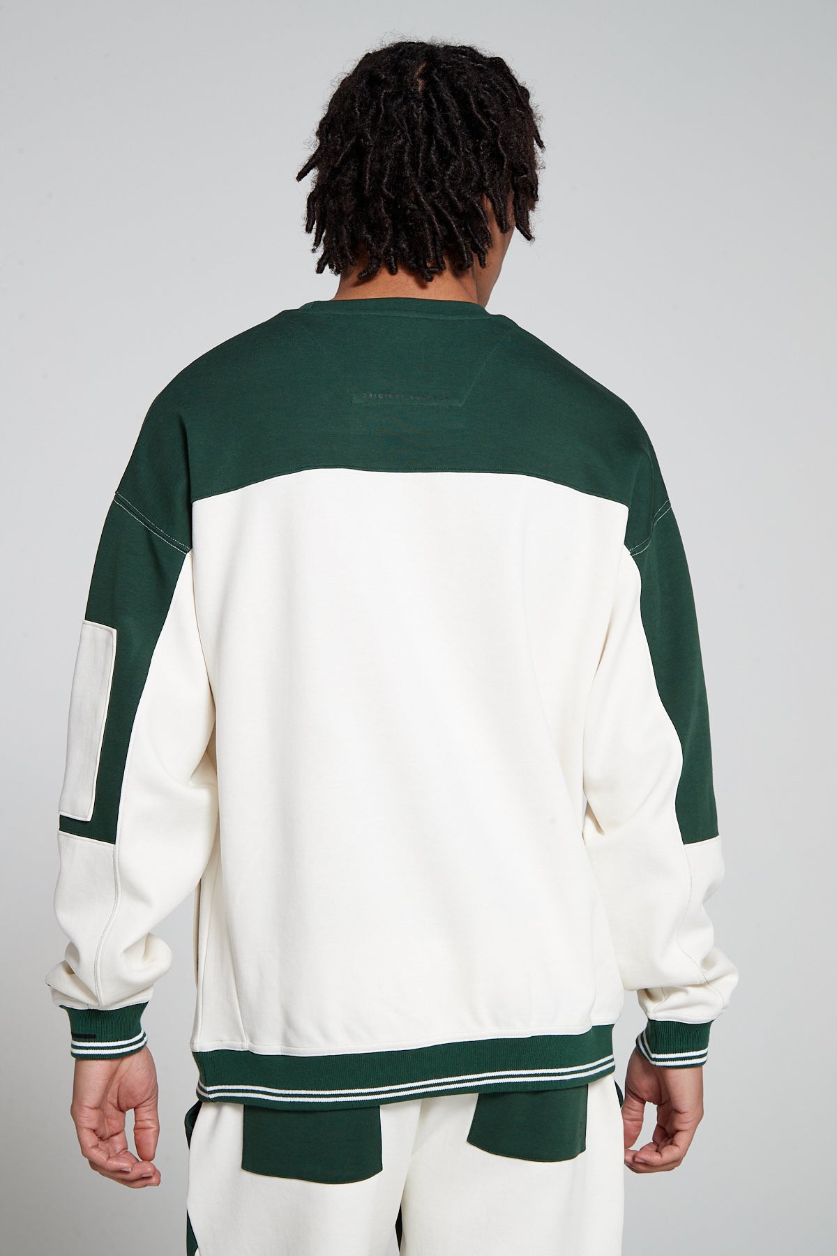 Model showing behind view wearing Oversized Original Creator Retro Zip pocket Sweatshirt in Varsity Green color with minimal branding at the back and color combination of Varsity Green and off white on sweatshirt. Showing off the complete set with Off white and Varsity Green retro shorts.