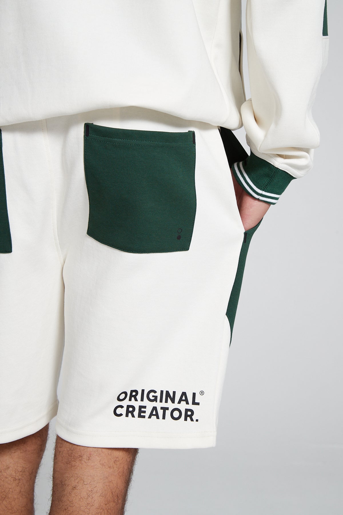 Model showing close up behind view wearing Original Creator Track 2.0 Retro zip pocket Shorts in Varsity Green with horizontal Original Creator branding at the bottom right corner. The shorts have green back pockets and white background