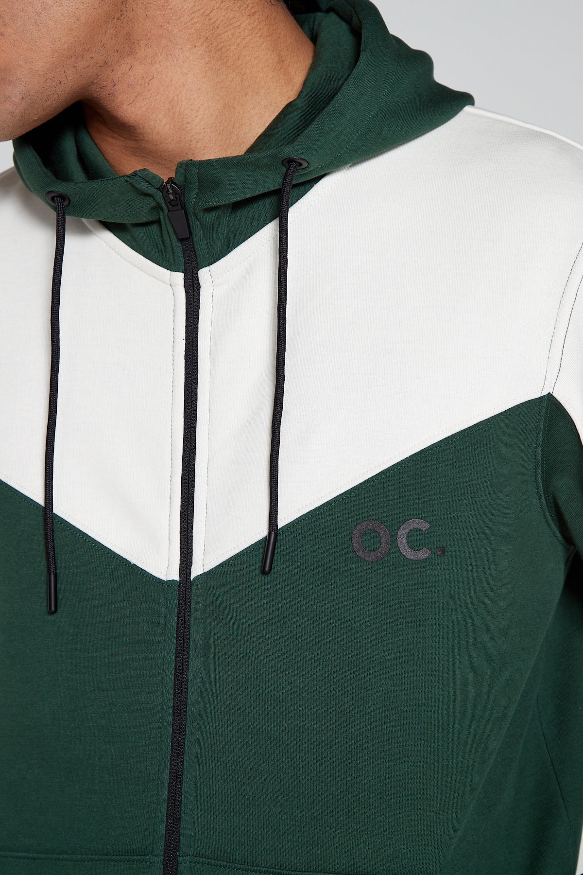 Close up center view of Original Creator Retro Zip Hoodie in Varsity Green color. Model Showing off the hoodie with closed zip along with minimal OC branding on upper left side of chest. Model is looking away showing off the unique white and Green color combination of hoodie