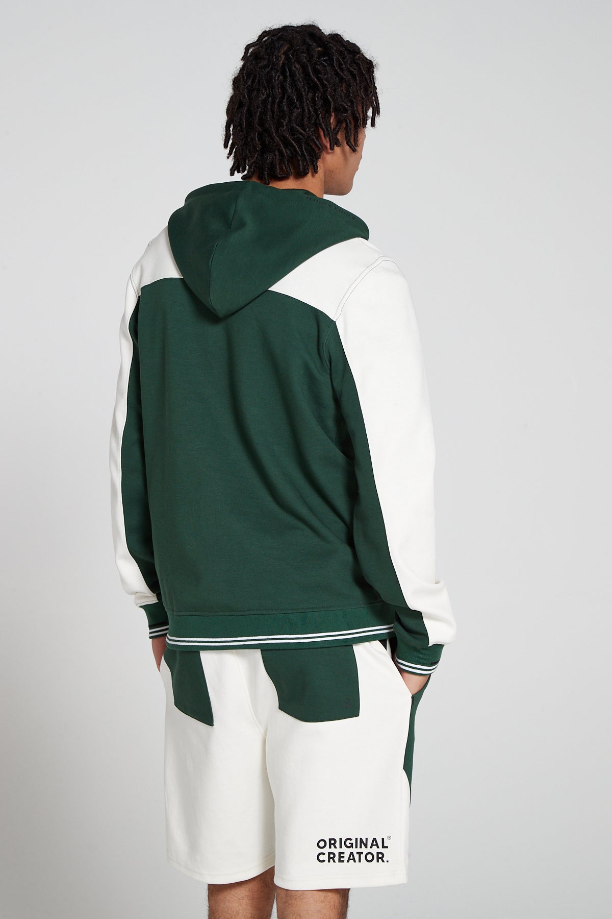 Model showing behind view wearing Original Creator Retro Zip Hoodie in Varsity Green color with no branding at the back and featuring water repellent technology and classic line pattern on the wrists and color combination of varsity green and Off white. Showing off the complete set with matching retro shorts