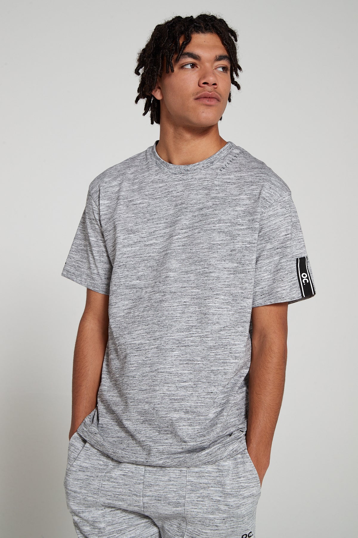 Model looking away wearing Original Creator Reflection T-Shirt in Granite Grey color with very no branding at the front. This T shirt features water repellent technology and OC brand tapping on left sleeve