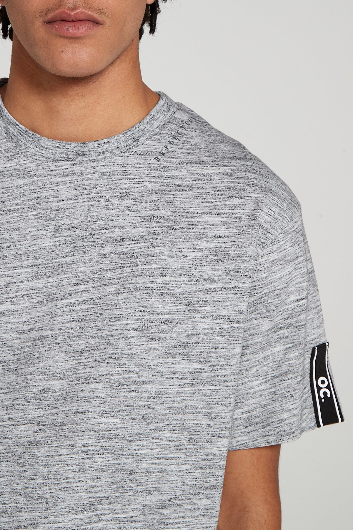 A close up front view of Original Creator Reflection T-Shirt in Granite Grey color front. The left sleeve has OC brand tapping and the round neck has the word Reflection printed