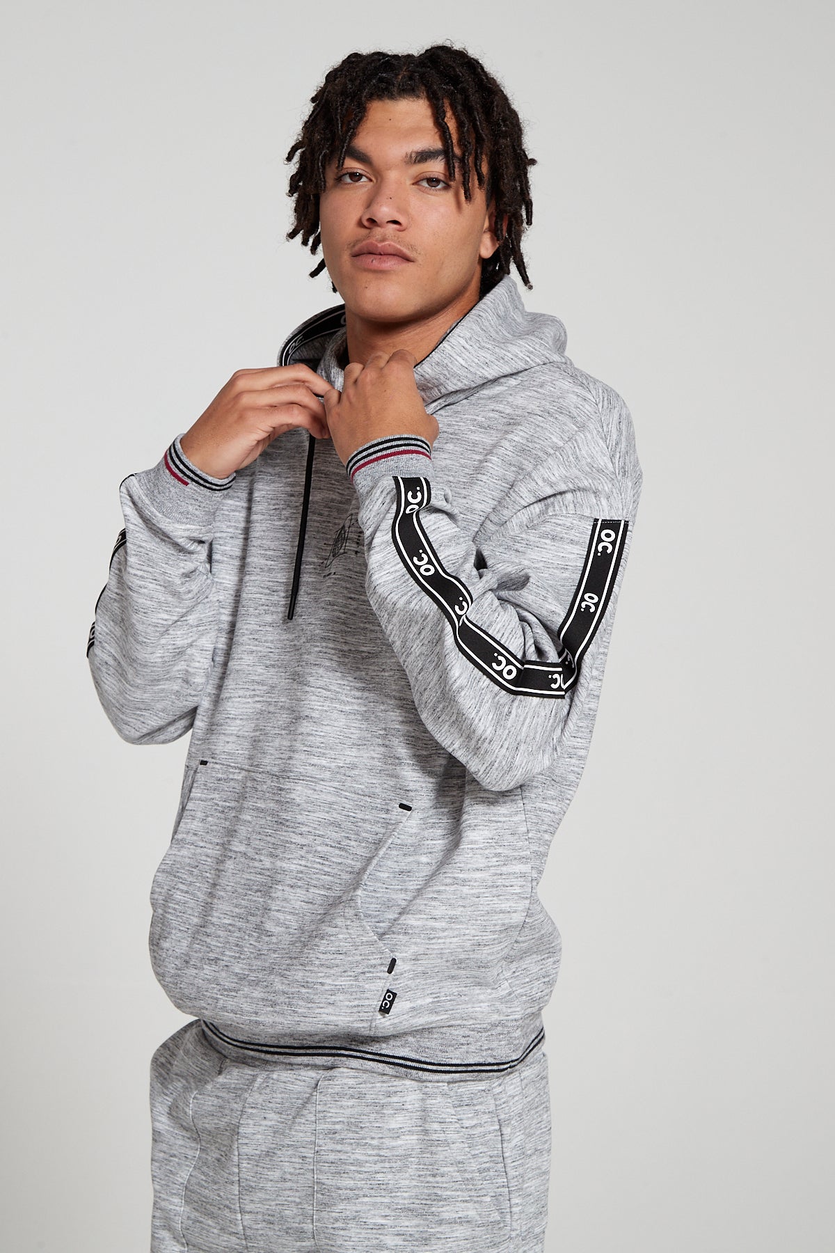 A close up view of model wearing Original Creator oversized Classic Hoodie in Granite Grey color highlighting the Signature OC taping finish on sleeves. Also showing kangaroo pocket along an additional hidden zipper pocket to protect phone and keys. 