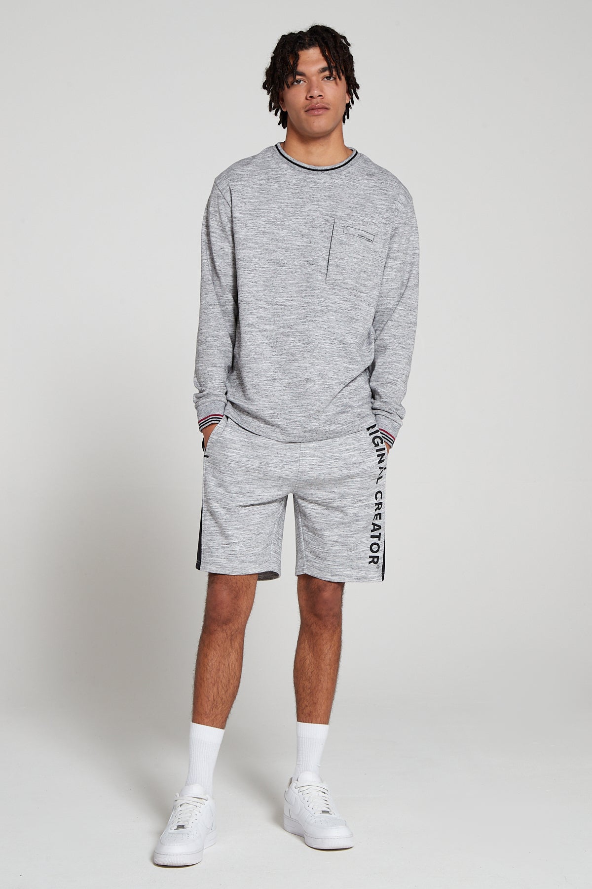 Full look of a model wearing Original creator Zip Pocket Long Sleeve Granite Grey T shirt with very low branding and features water repellent technology zip pocket along a matching set of Original creator retro Granite Grey shorts and hand in the shorts pockets