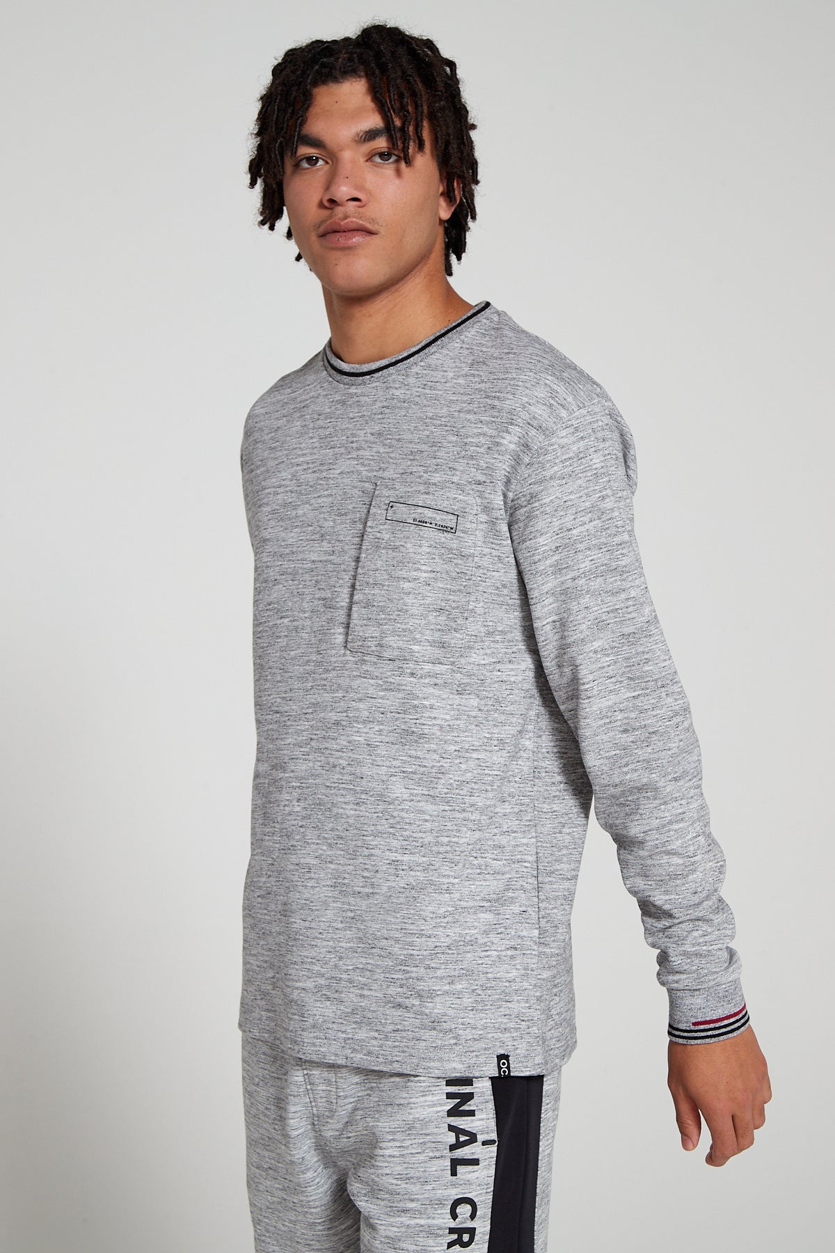 Model looking Straight wearing Original Creator oversized Granite Grey Long sleeve T shirt with minimalistic branding and features water repellent technology and zip pocket arms moving freely showing off sleeves