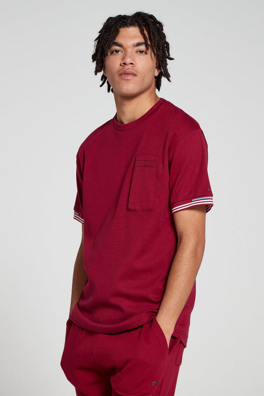 Model looking Straight wearing Original Creator oversized Olympic Cranberry Red T shirt with very low branding and features water repellent technology zip pocket 