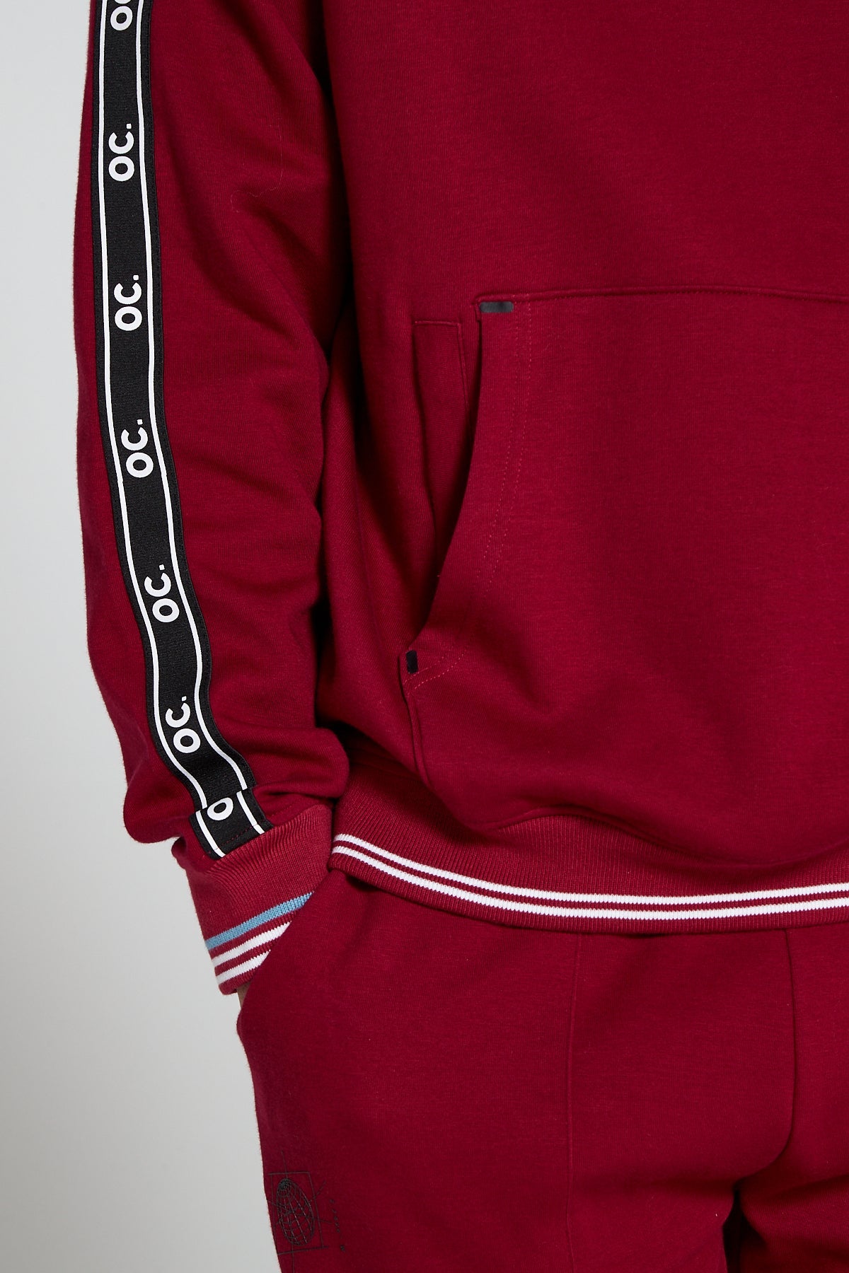 A close up view of model wearing Original Creator oversized Classic Hoodie in Cranberry Red color highlighting a kangaroo pocket along with a hidden zipper pocket to protect phone and keys. Signature OC taping finish on sleeves to add a classy touch