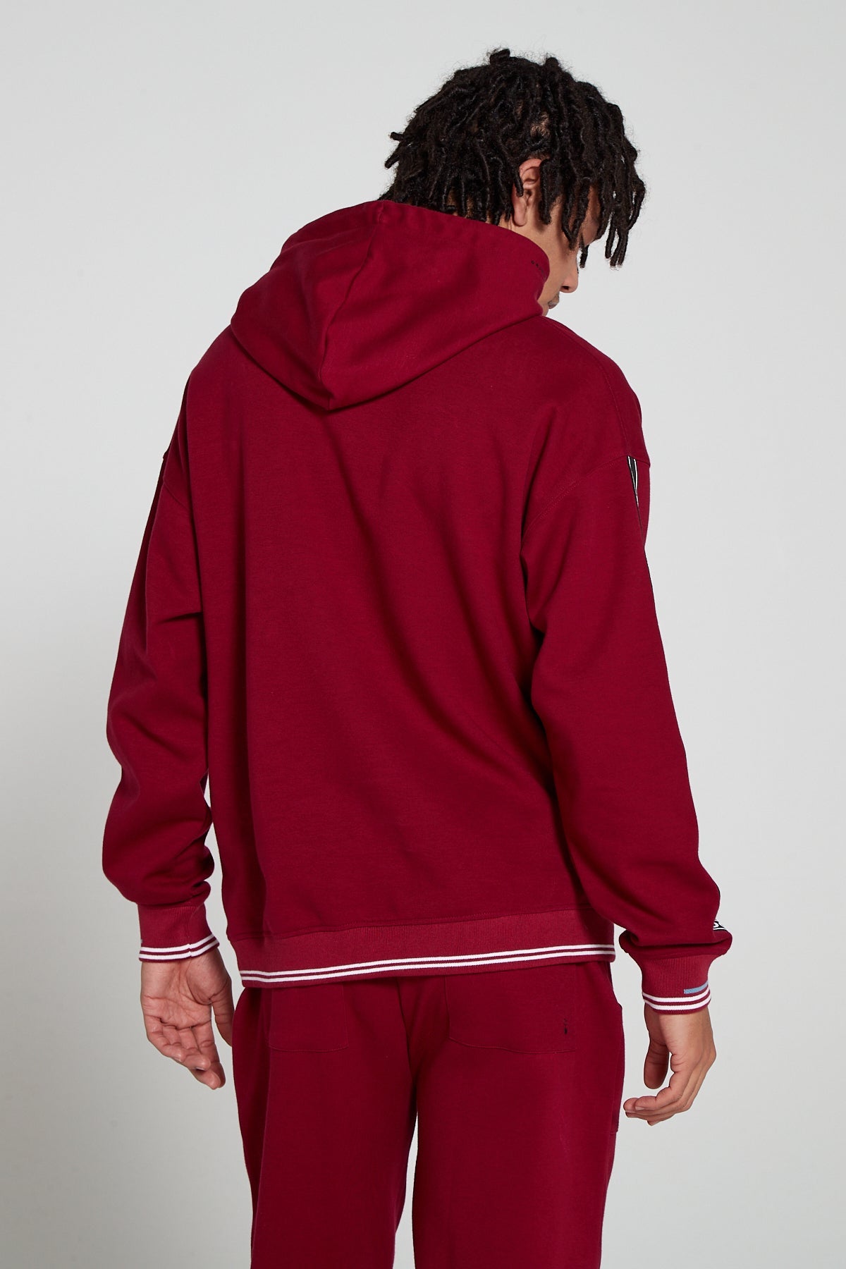 Model showing behind view wearing Original Creator oversized Classic Hoodie in Cranberry Red color with no branding at the back and featuring water repellent technology and classic line pattern on the sleeves