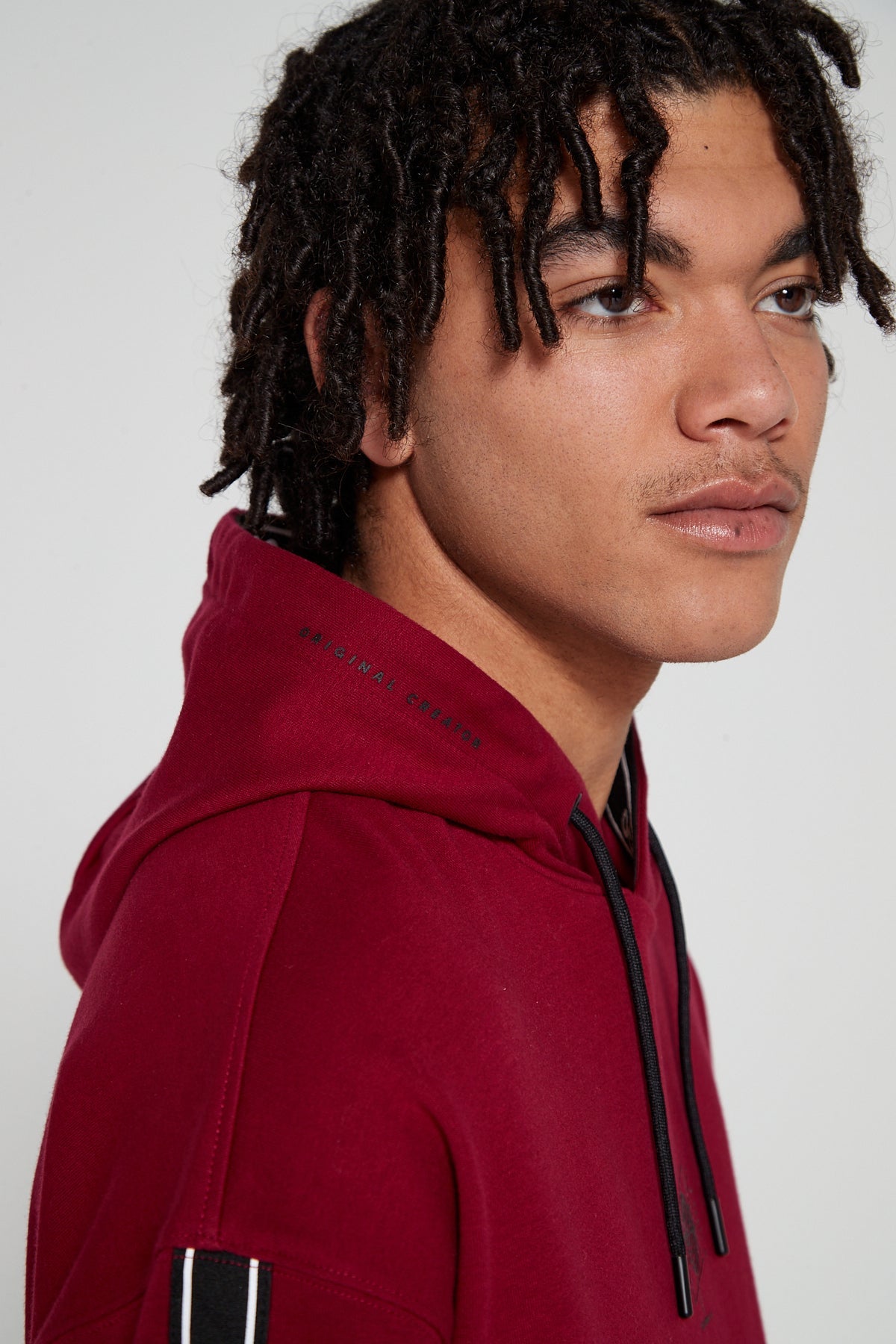 Model looking away showing side view wearing oversized Original Creator  Classic Hoodie in Cranberry Red color with Minimalist branding on the hood