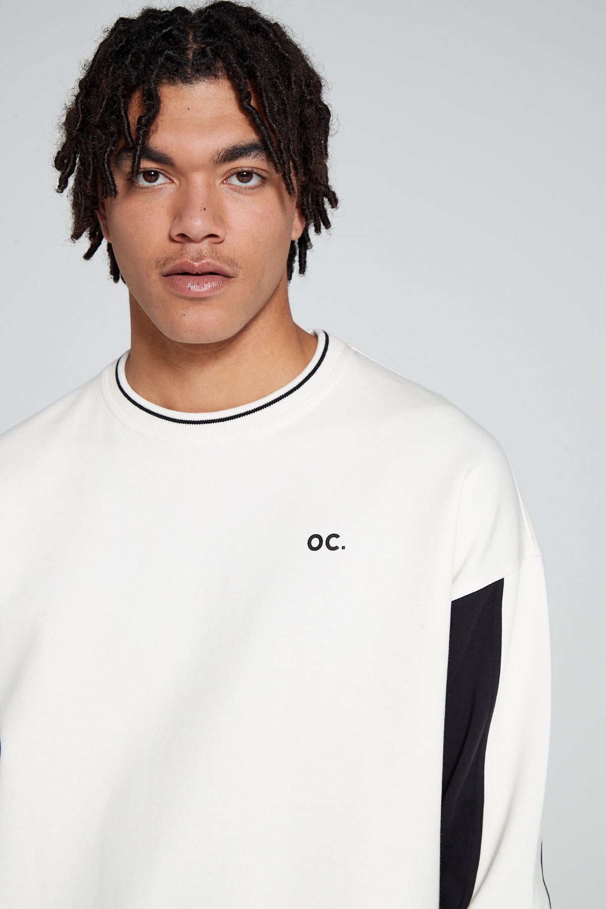 Close up top center view of Original Creator Retro Sweatshirt in Off White color. Minimal OC branding on upper left side of chest. Model is looking straight showing off the unique black and white color combination on sweatshirt