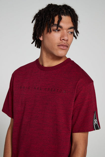 Model showing OC tag on sleeve and looking down wearing Original Creator oversized  Red T shirt with minimalistic branding and features water repellent technology