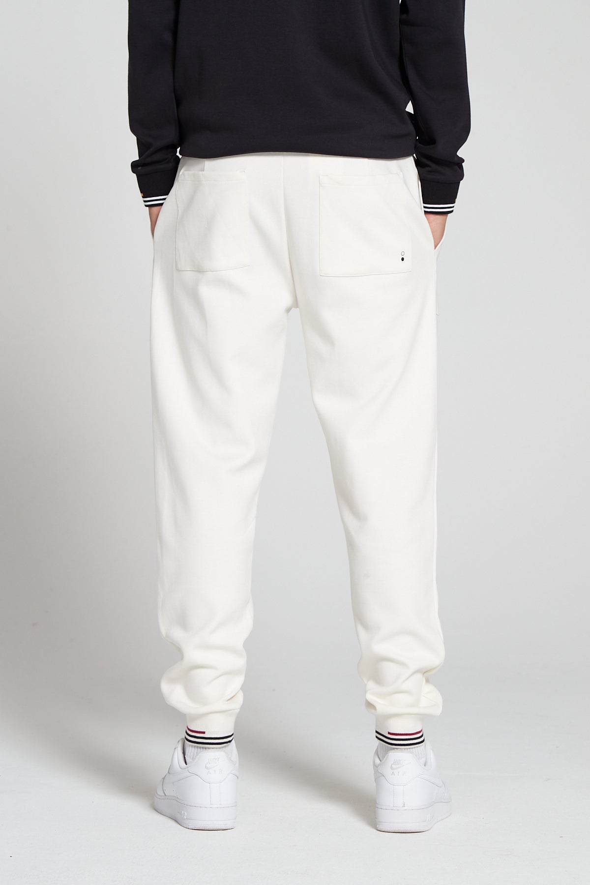 Model showing a behind view wearing Original Creator Track 2.0 Classic Joggers in Off white Color with plain look at the back. Features two pockets at the back and black and red lining on ankles